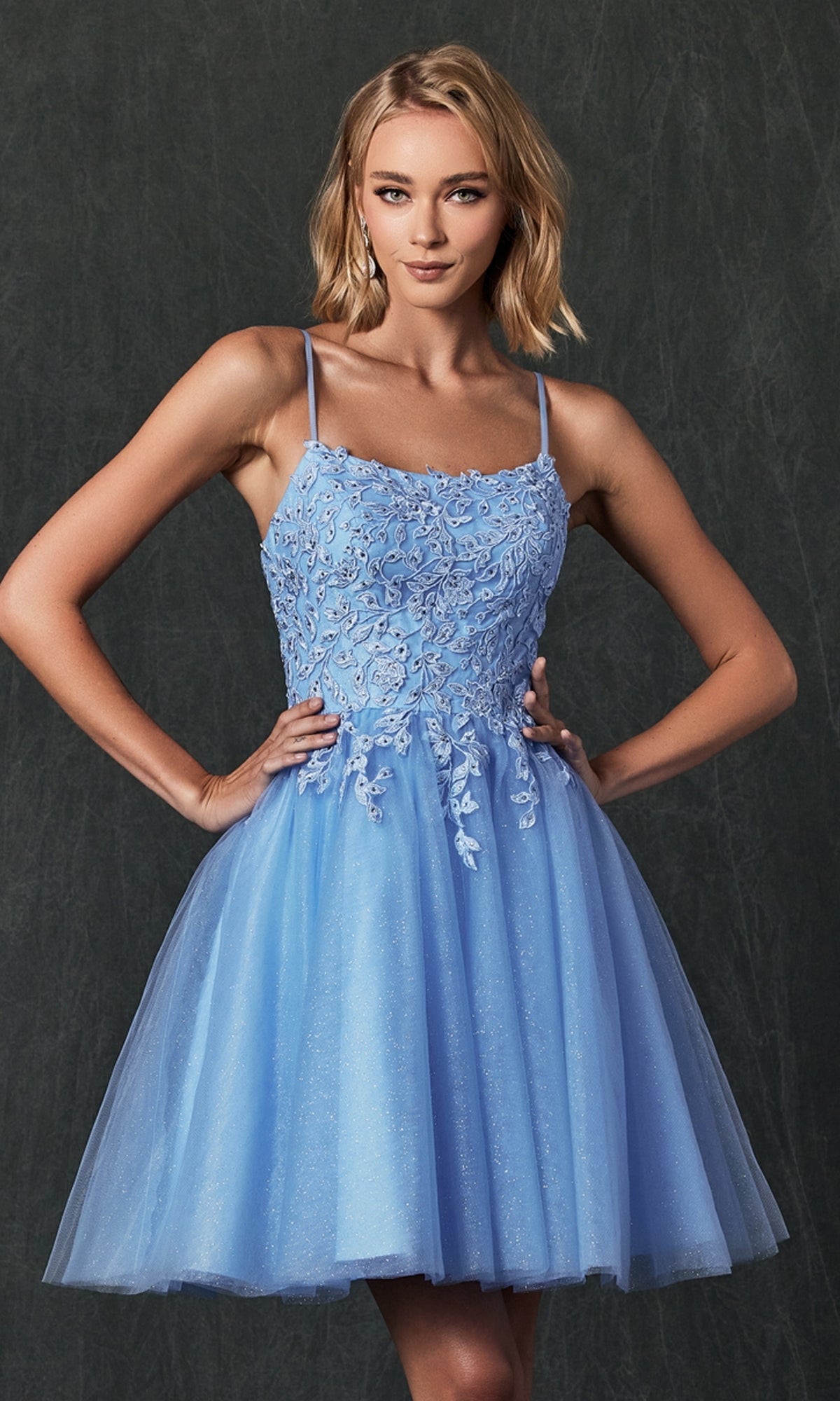 A woman wears the Embroidered-Corset Babydoll Homecoming Dress 860, a light blue, sleeveless short dress with floral lace bodice detailing, standing against a dark background.